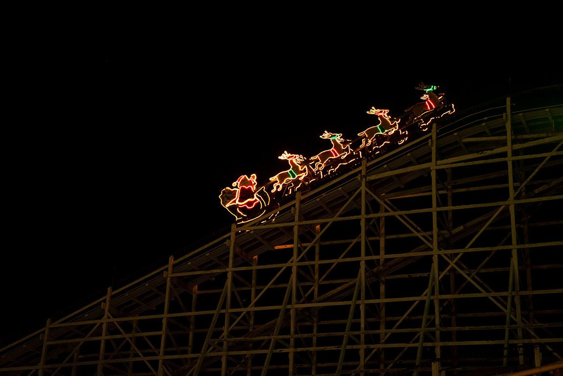 A view of Hersheypark at Christmas, with a lit-up rollercoaster decorated with reindeer and Santa.