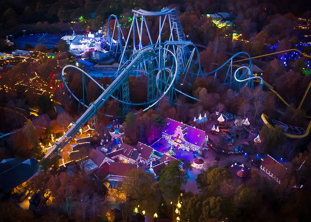 Aerial view of a brightly lit roller coaster and surrounding buildings decorated for the holidays at night, showcasing Christmas Williamsburg VA.