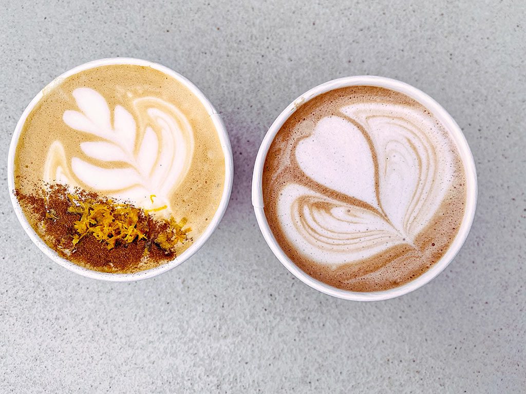 An Orange Raspadura Latte sits on the left, distinctive with its unique hue, next to a rich, dark hot chocolate, both served in mugs at Cafe Unido in La Cosecha. This delightful pair highlights a spot that could be serving the best hot chocolate near me or the best hot chocolate in dc.