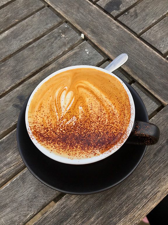 A black mug filled with steaming hot chocolate, generously sprinkled with cinnamon, sits on a matching black coaster. This inviting presentation suggests a delicious find for anyone seeking the best hot chocolate near me or the best hot chocolate in dc.