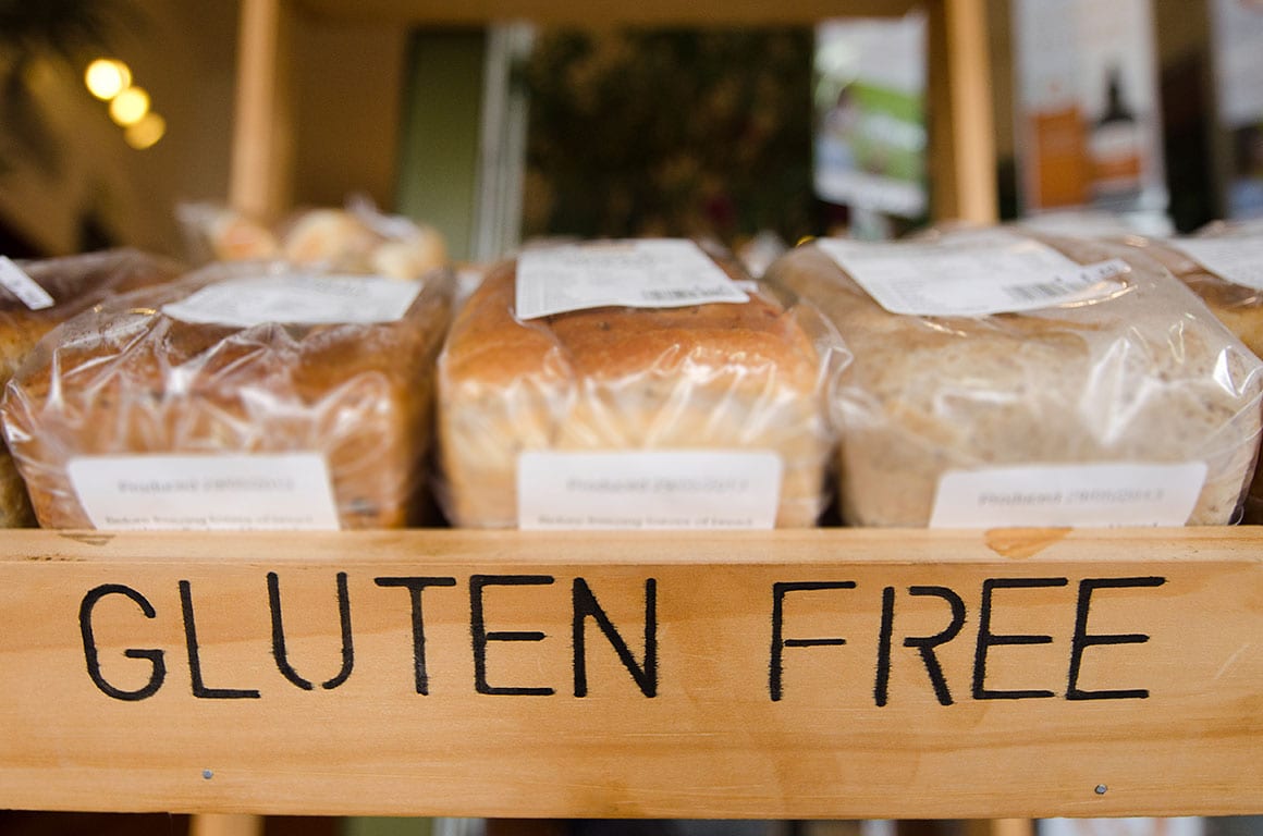 Close-up shot of three packaged loaves of bread on a wooden shelf. The bread appears to be gluten-free, with "GLUTEN FREE" clearly written on the shelf. This could be a representation of the types of products found in gluten free bakeries DC.