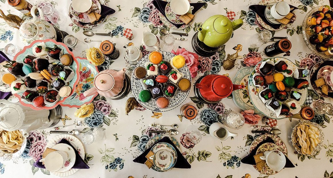 An overhead shot of a beautifully set table for afternoon tea Washington DC, featuring colorful teapots, plates of macarons and pastries, and teacups arranged on a floral tablecloth.