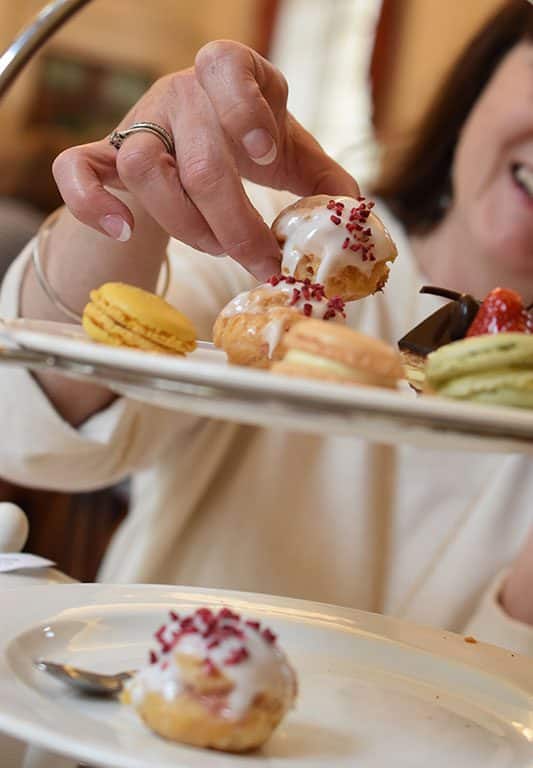 A woman's hand reaches for a delicate pastry from a tiered stand, part of an afternoon tea Washington DC experience. The stand holds colorful macarons and other small treats.