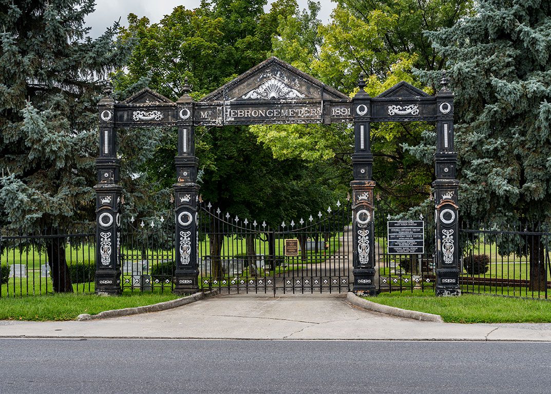The ornate, historic entrance gate to Mount Hebron Cemetery in Winchester, Virginia, featuring decorative black ironwork with the words "MT HEBRON CEMETERY 1891" prominently displayed, suggesting a place of historical interest for things to do in Winchester VA.