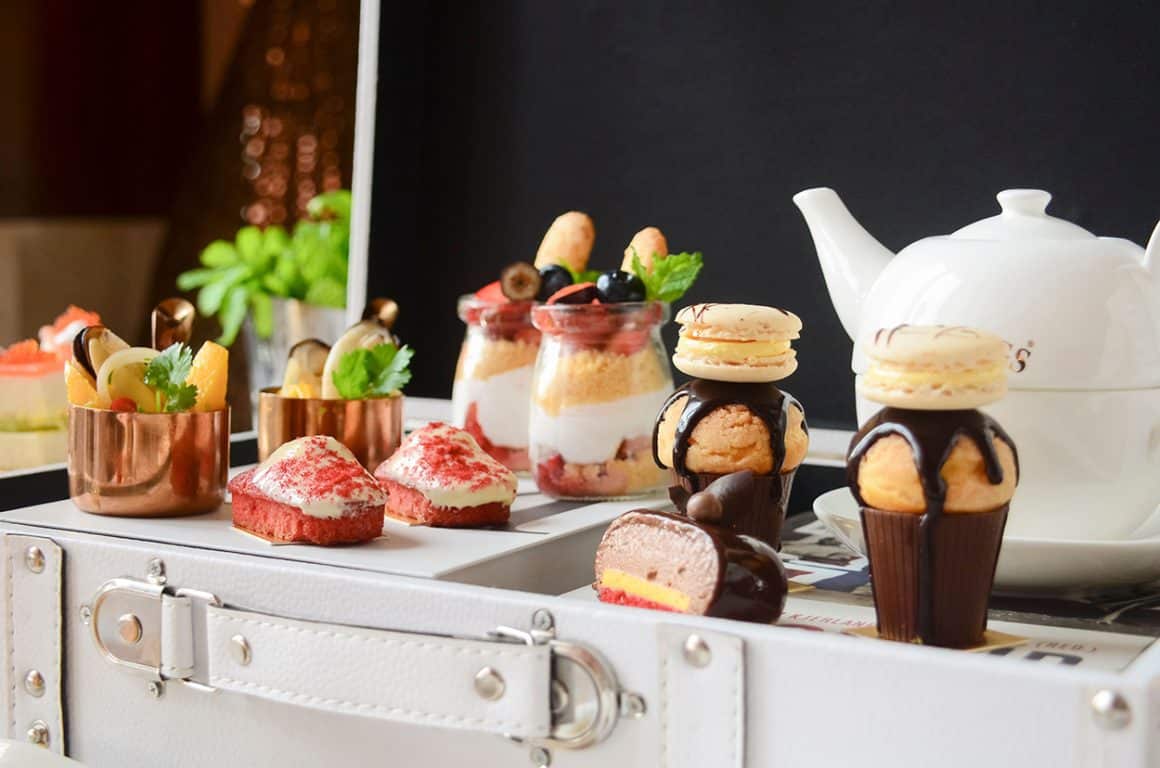 This image shows a whimsical afternoon tea setup, reminiscent of a kids afternoon tea experience, with colorful mini desserts and treats arranged in a suitcase-style serving tray, similar to what you might find at an afternoon tea Washington DC event.